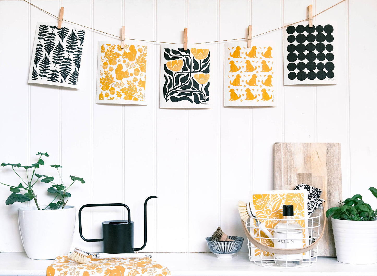 Decorative prints with patterns on a white wall with a table and plants below.