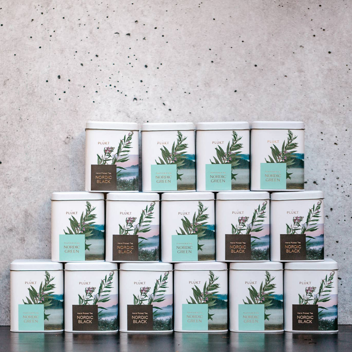 Stack of tea tins with green leaf design against a gray concrete wall