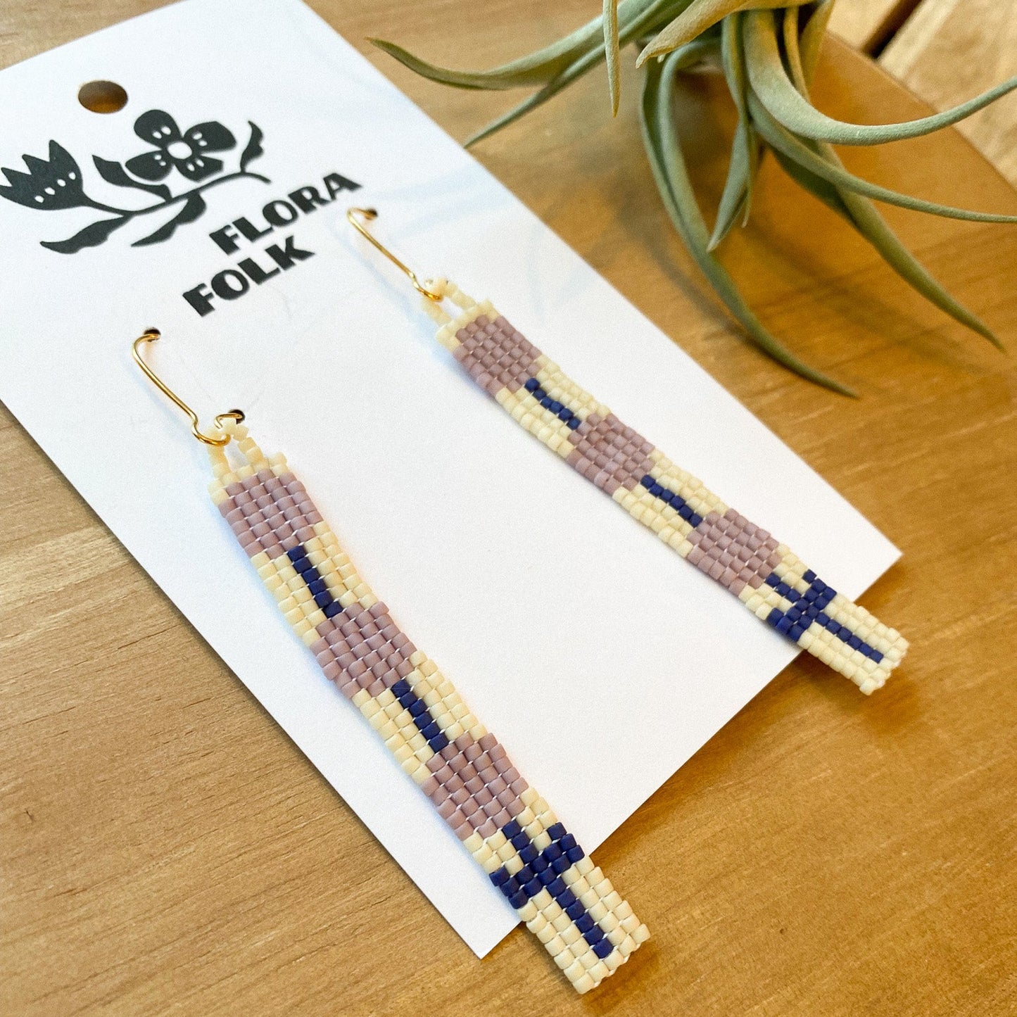 Beaded earrings on a 'Flora Folk' branded card with a plant in the background