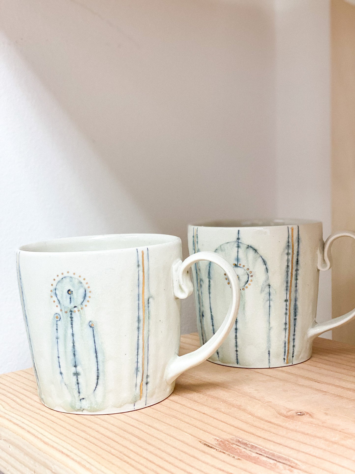 Two ceramic mugs with abstract designs on a wooden surface.