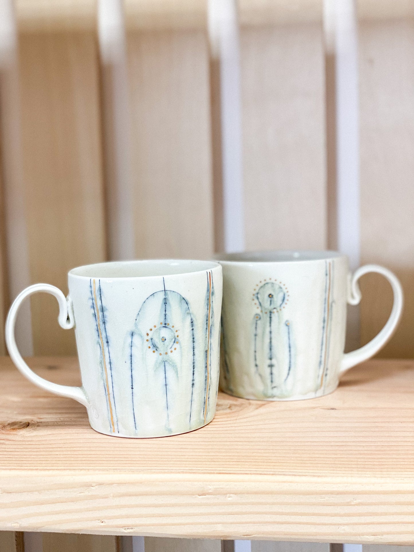 Two ceramic mugs with abstract designs on a wooden surface