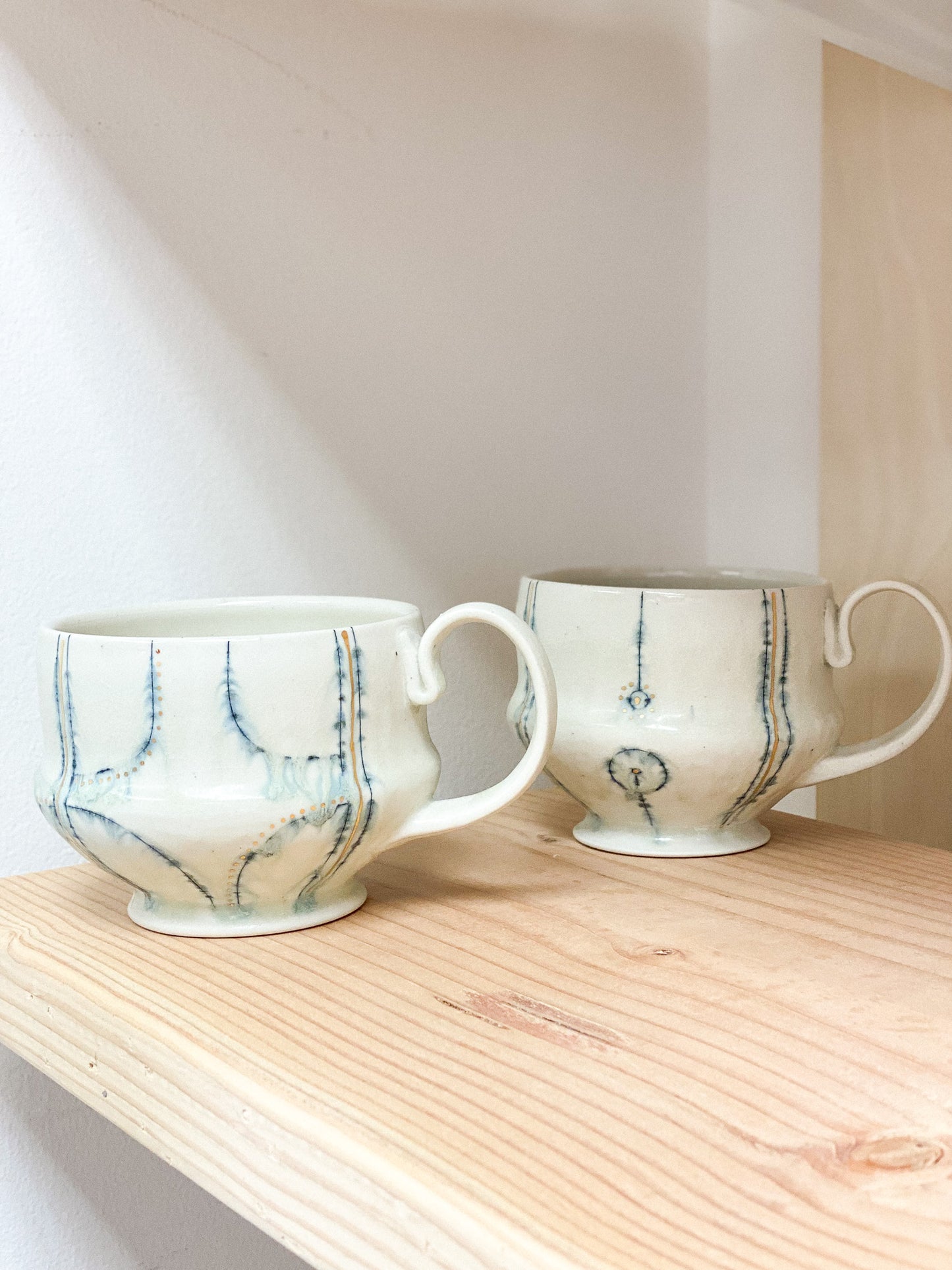 Two ceramic mugs with abstract patterns on a wooden shelf.
