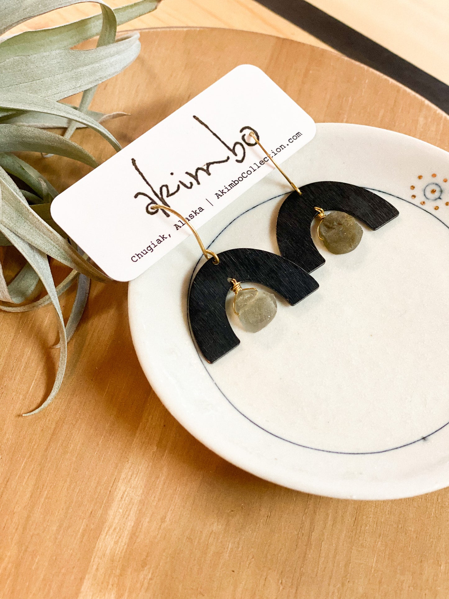 Black arch-shaped earrings with gold accents on a white dish, with a plant in the background.