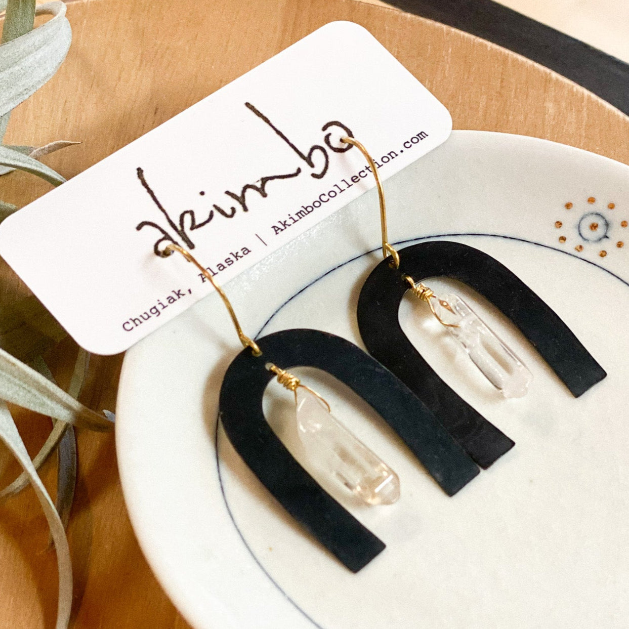Black arch-shaped earrings on a white dish with a plant in the background