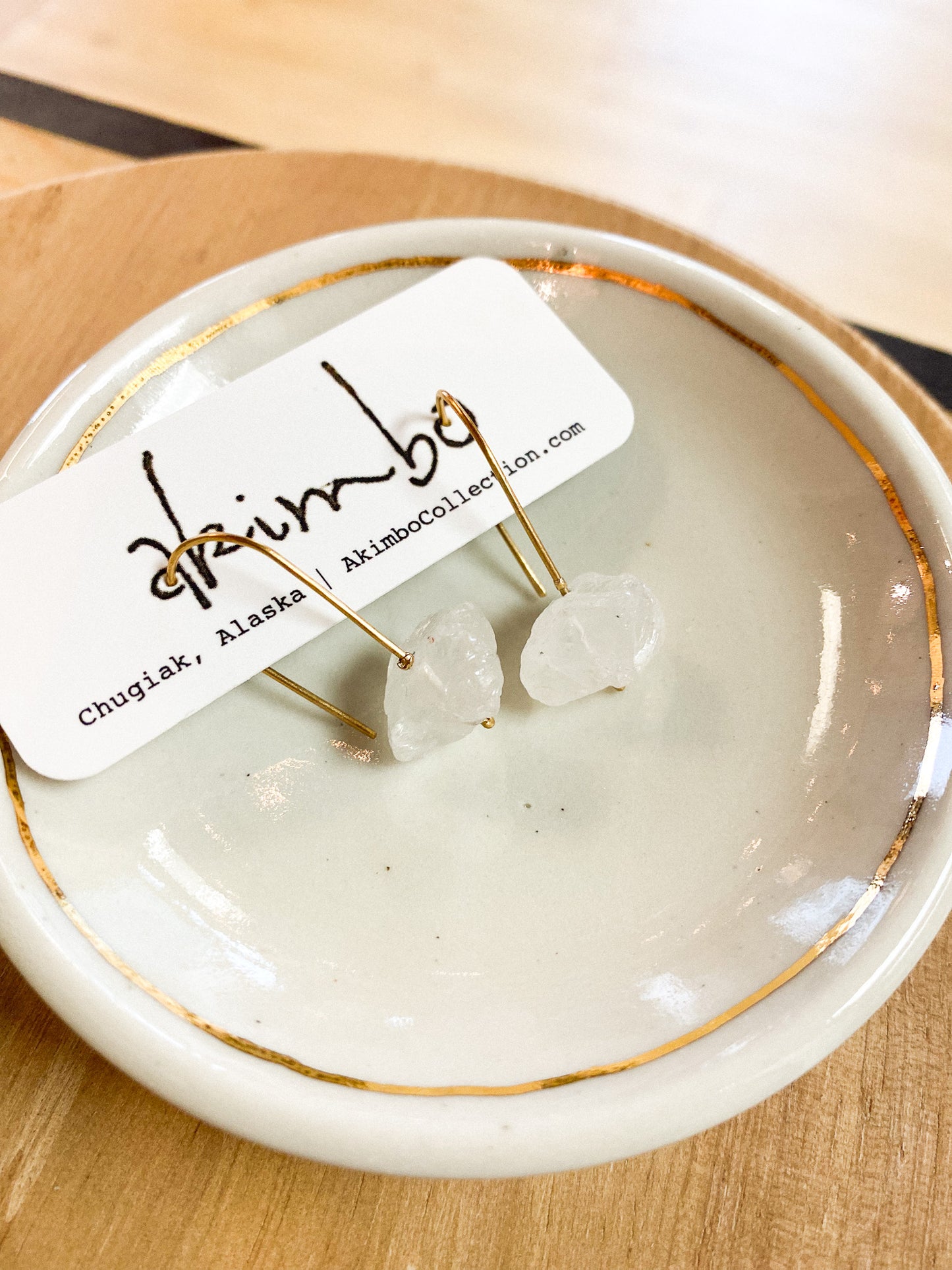 Earring set on a white dish with a 'akimbo' label, on a wooden surface