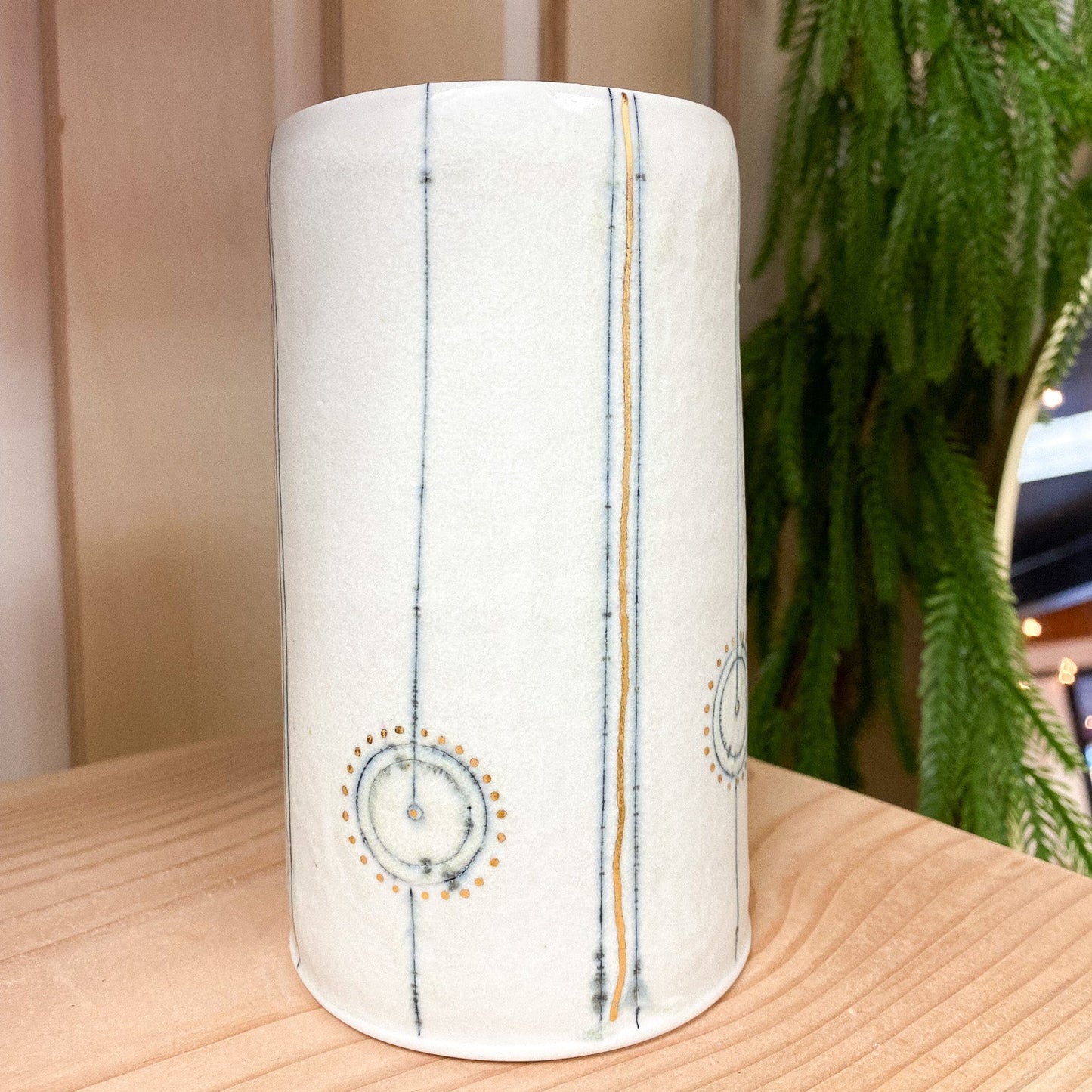 Cylindrical ceramic vase with decorative patterns on a wooden surface