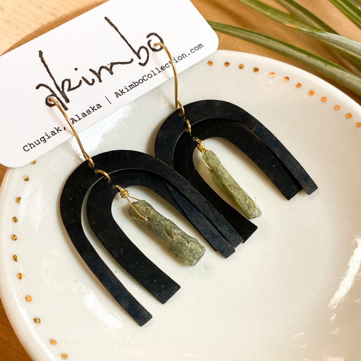 Black and green earrings on a white dish with a plant in the background