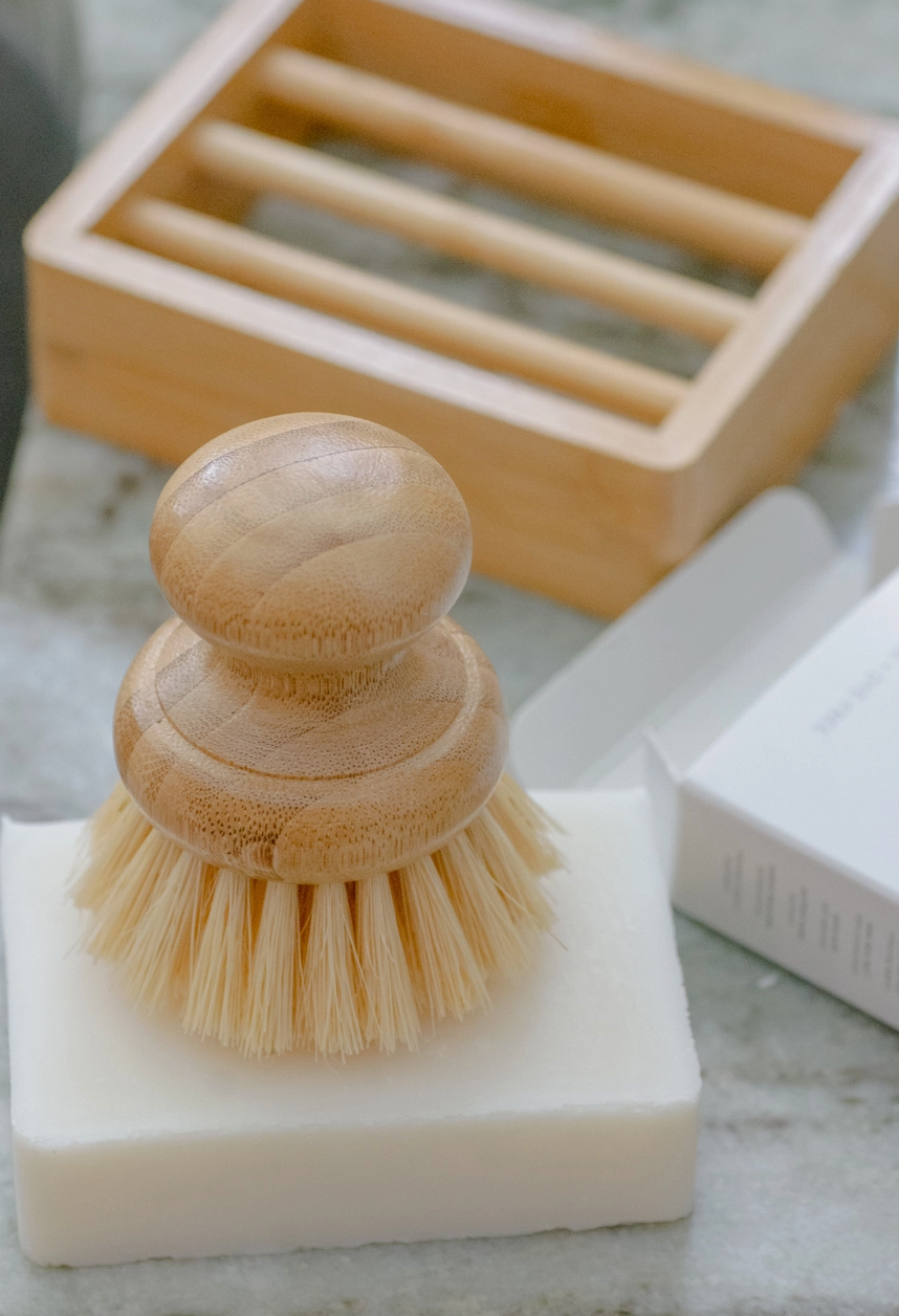Wooden dish brush on a bar of soap with a wooden soap dish in the background.