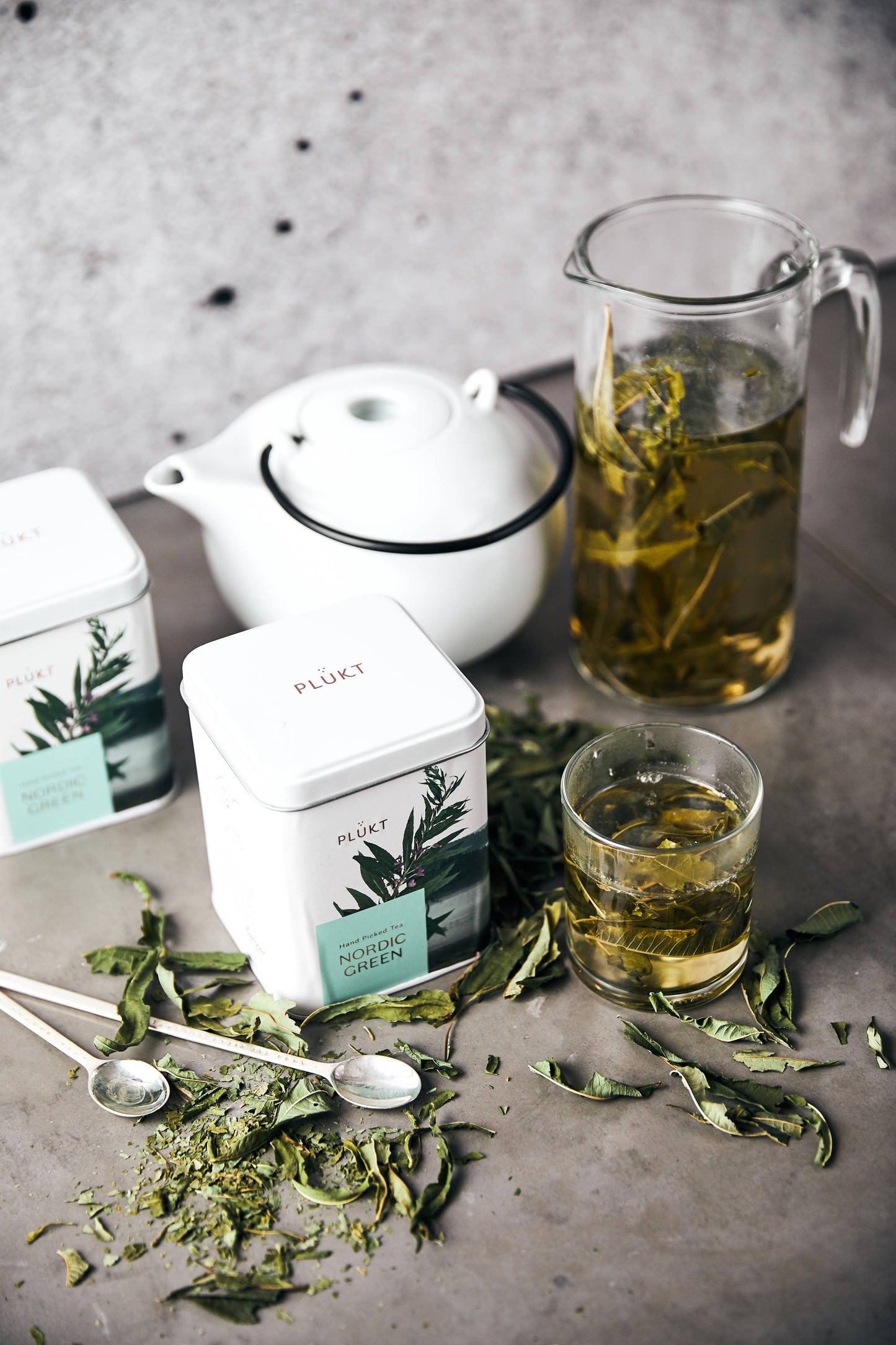 Tea-making setup with teapot, glass, and tea leaves on a gray surface