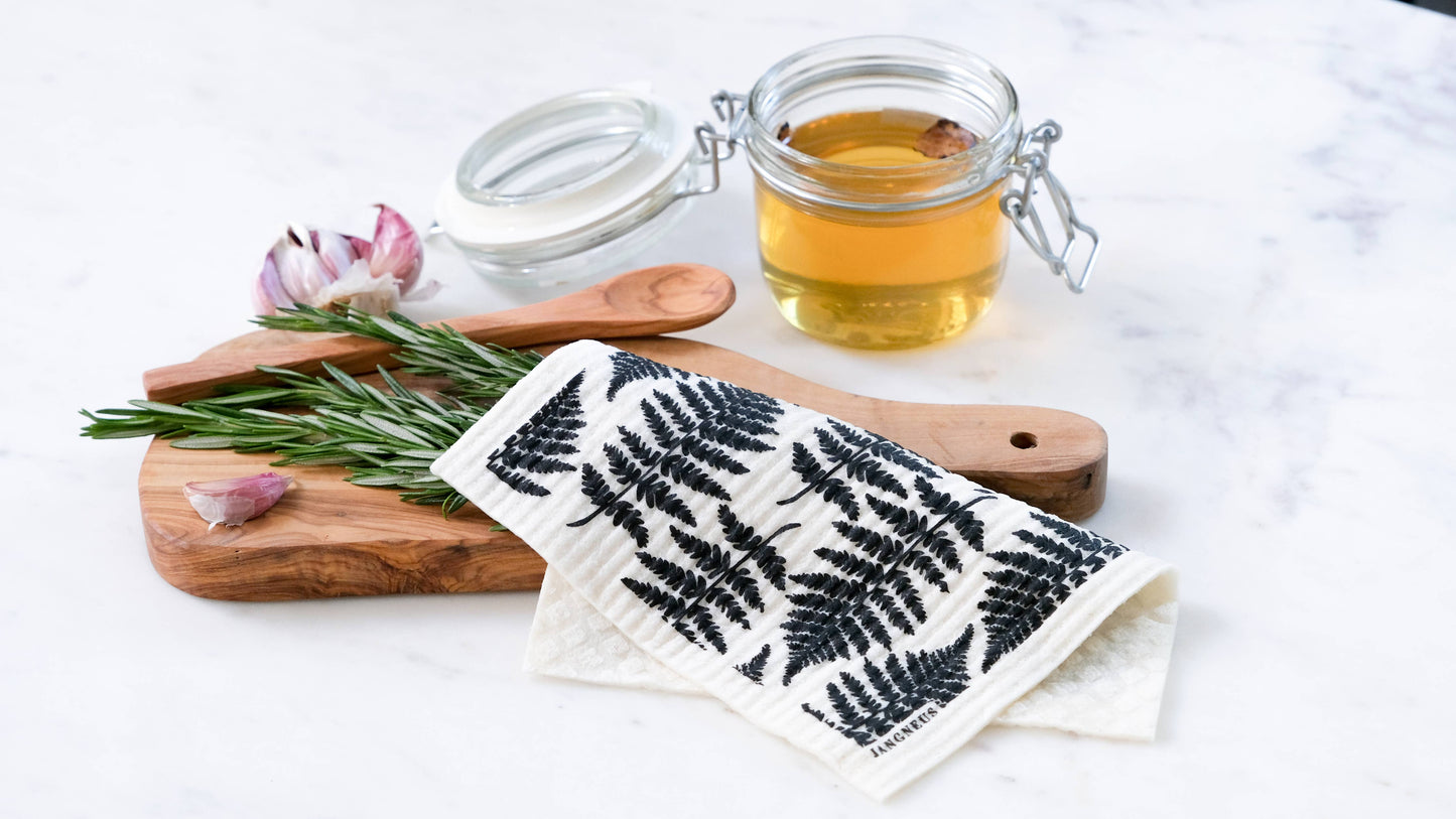 Fern-patterned cloth on a wooden cutting board with herbs and a jar of honey.