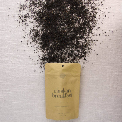 Tea packaging labeled 'Alaskan Breakfast' with scattered tea leaves on a textured surface