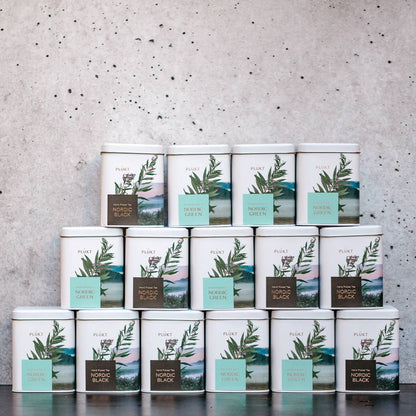 Stack of tea tins with green leaf design against a gray concrete wall