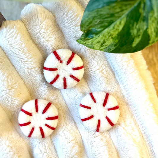 Three peppermint-shaped magnets on a soft white blanket with green leaves in the background