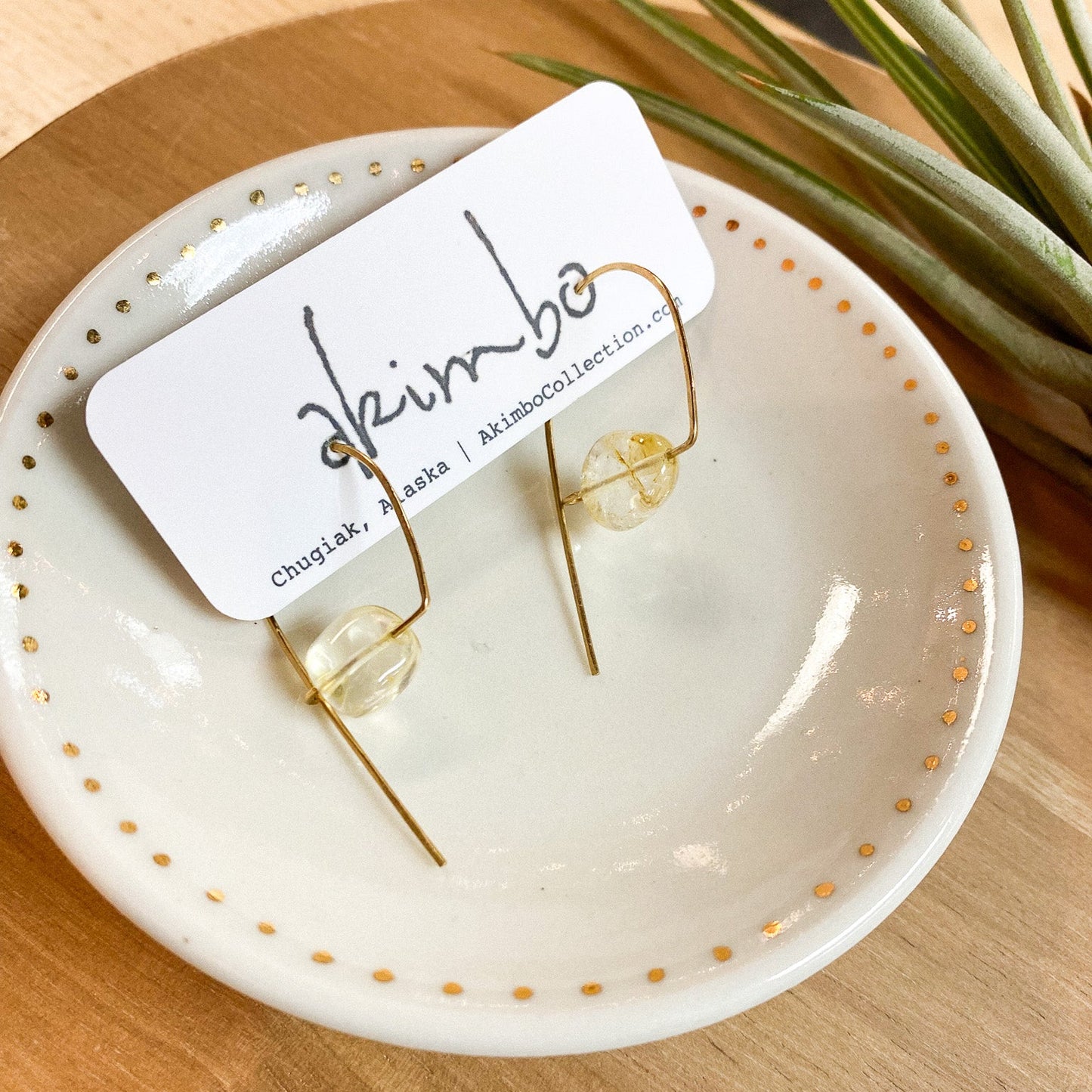 Gold hoop earrings on a white dish with gold polka dots, placed on a wooden surface with a plant in the background.
