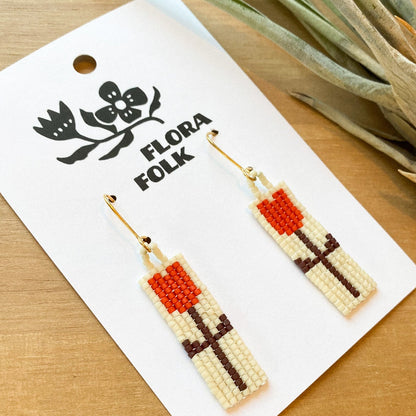 Floral patterned earrings on a 'Flora Folk' branded card with a plant in the background.