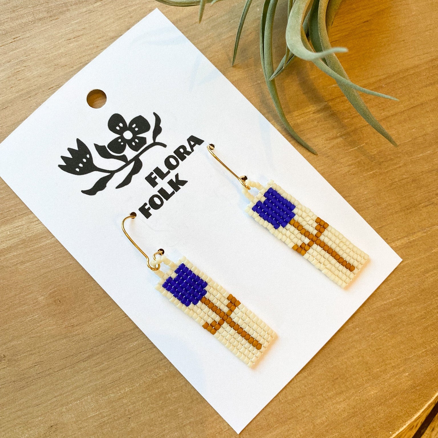 Beaded earrings on a 'Flora Folk' branded card with a plant in the background.