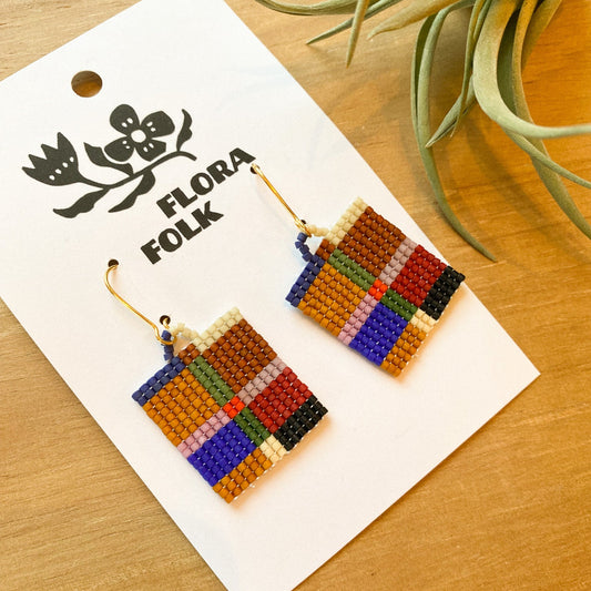 Colorful beaded earrings on a 'Flora Folk' branded card with a plant in the background.