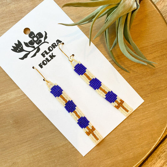 Mustard and blue earrings by Flora Folk with a plant in the background