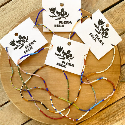 Colorful beaded bracelets on a wooden board with 'Flora Folk' tags.