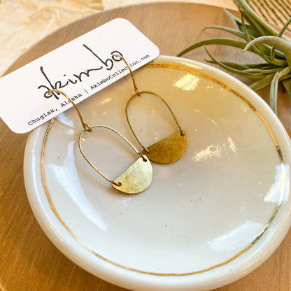 Gold hoop earrings on a white dish with a visible brand tag, placed on a wooden surface.