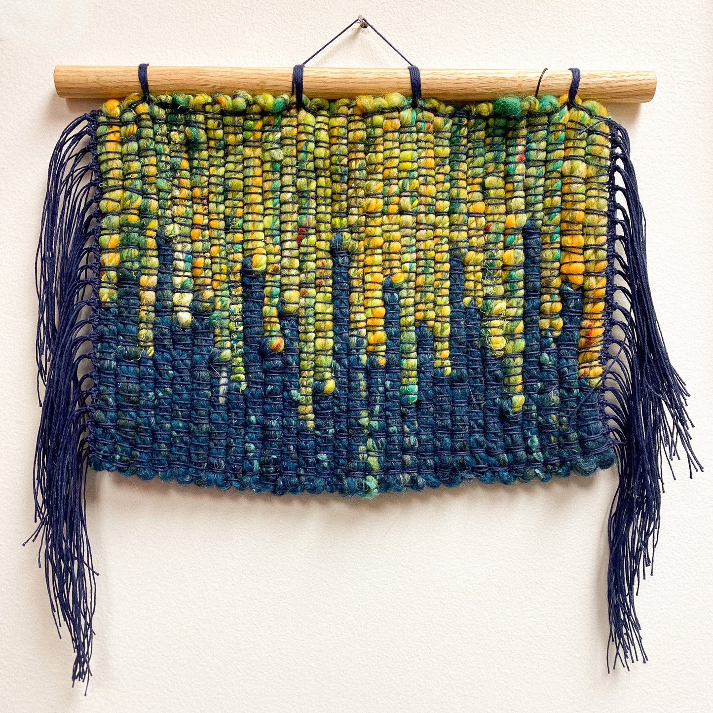 Woven wall hanging with blue and green aurora gradient on a white background