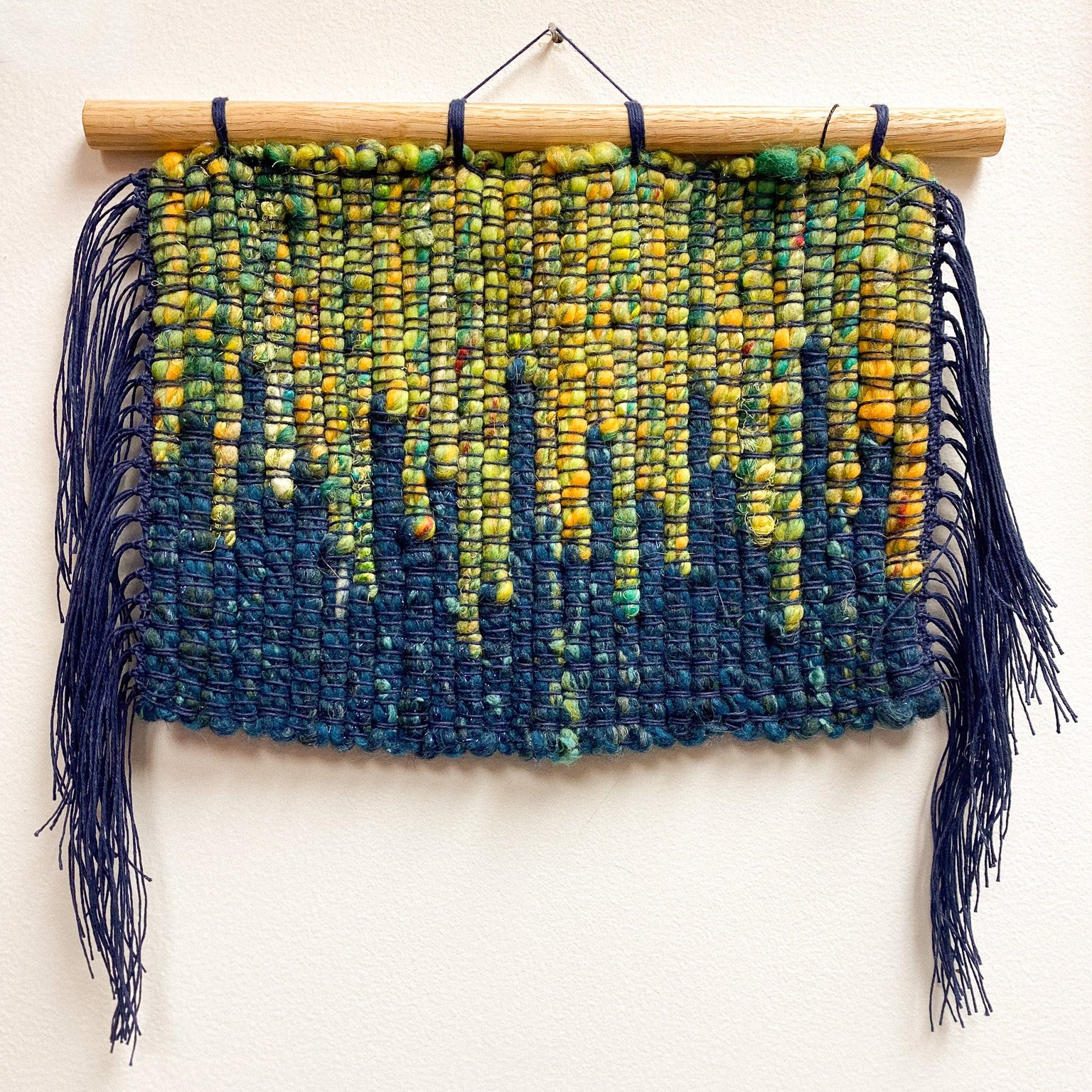 Woven wall hanging with blue and green aurora gradient on a white background