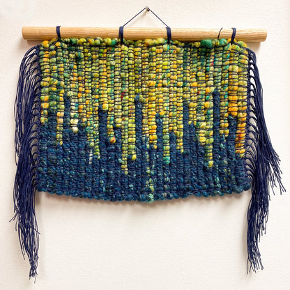 Woven wall hanging with blue and green aurora gradient on a white background