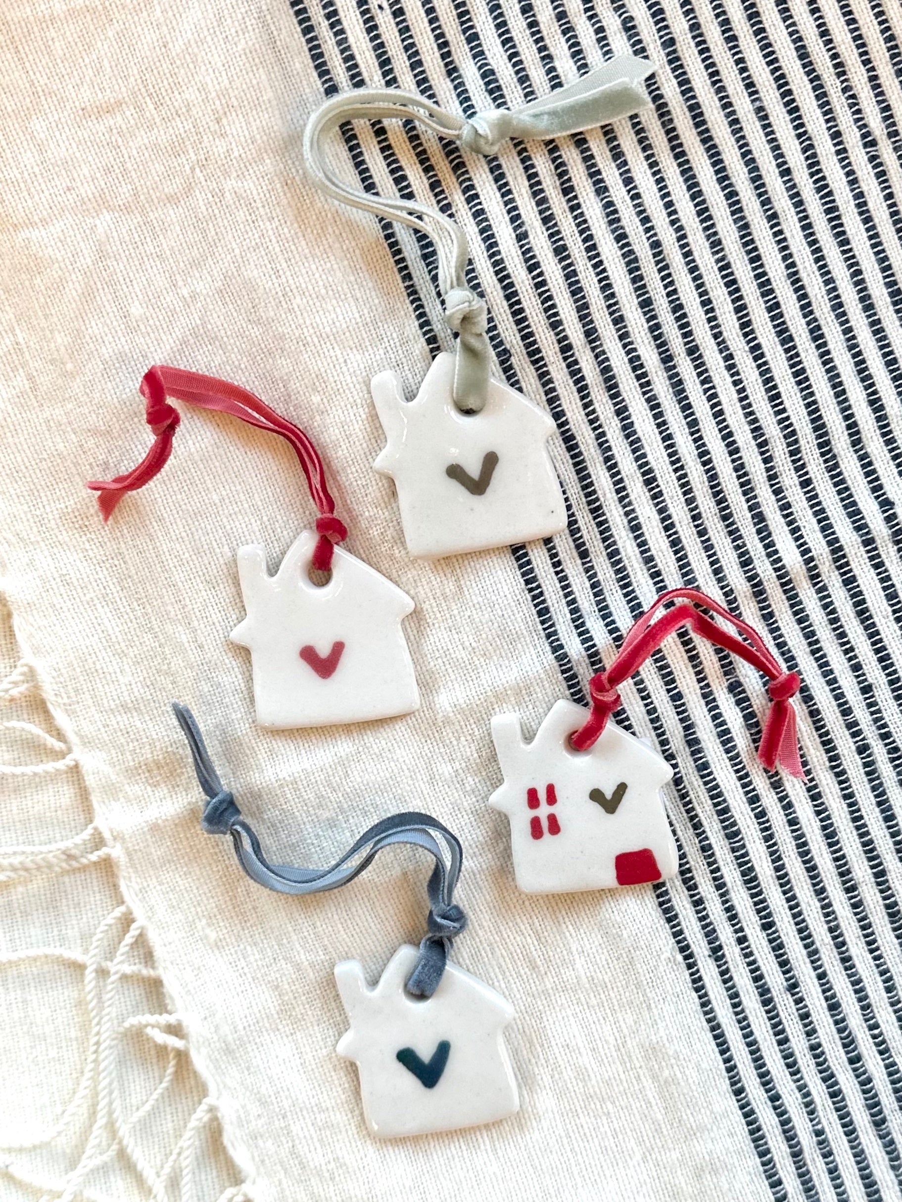 Decorative house-shaped ornaments with red ribbons on a striped fabric background