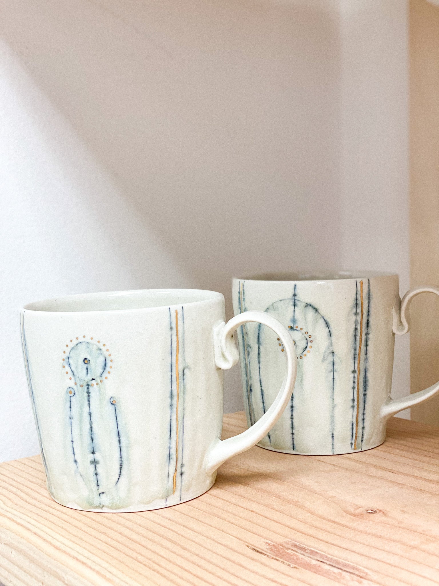 Two ceramic mugs with abstract designs on a wooden surface.