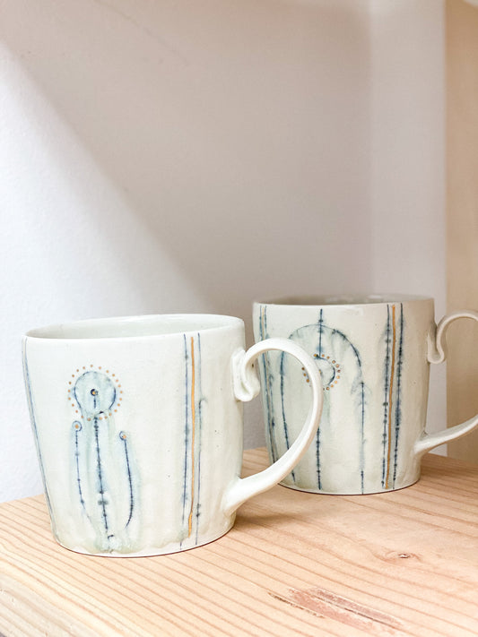 Two ceramic mugs with abstract designs on a wooden surface.