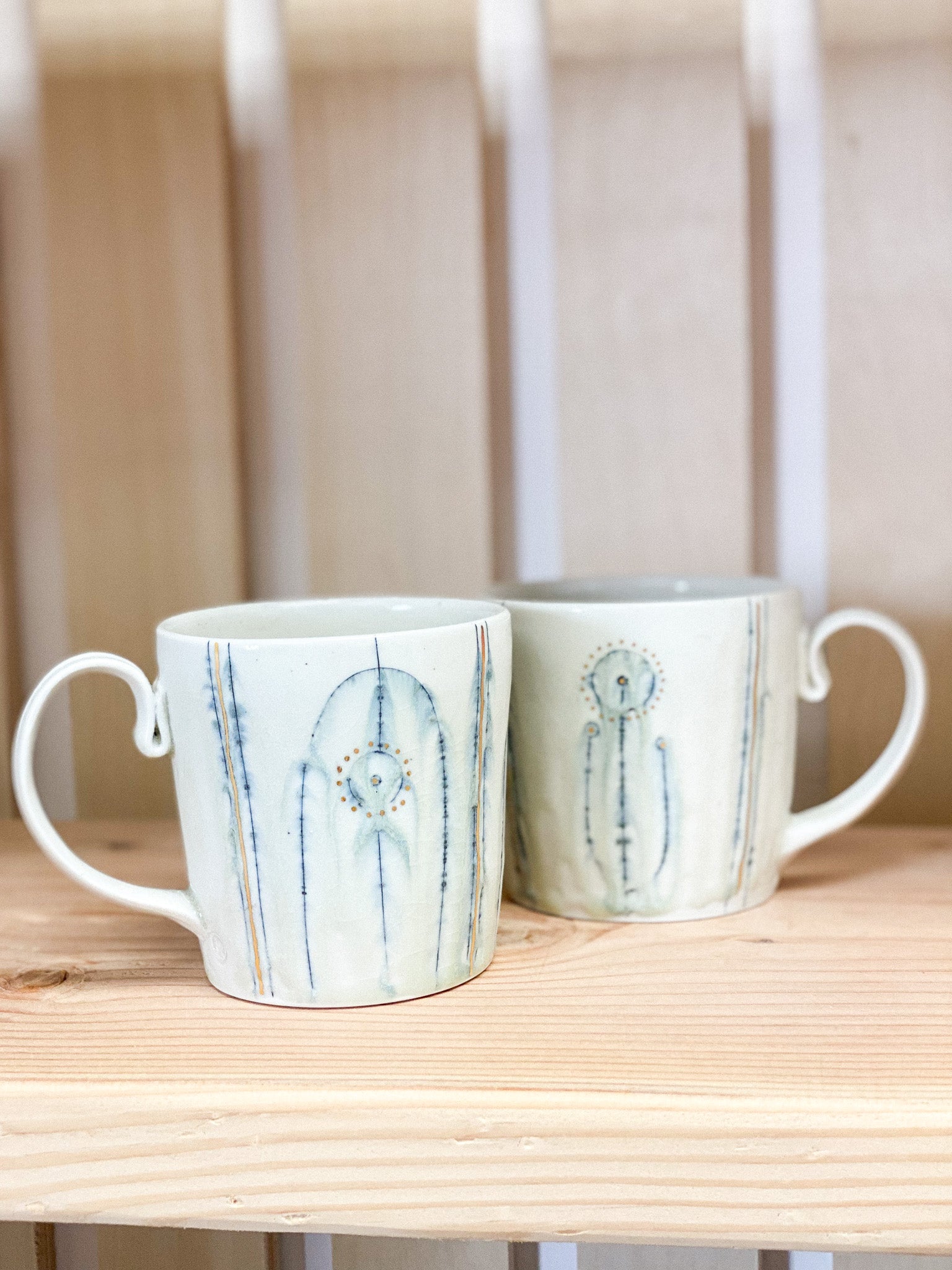 Two ceramic mugs with abstract designs on a wooden surface