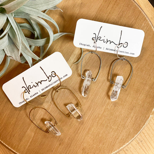 Clear glass earrings on a wooden surface with 'akimbo' branding.