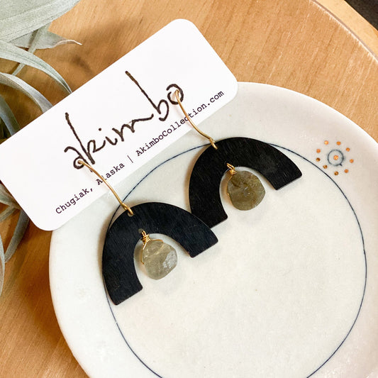 Black and gold earrings on a white dish with 'Akimbo' branding.