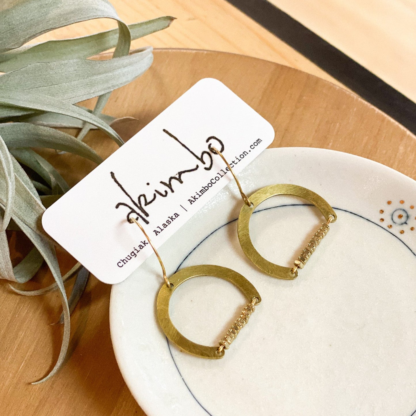 Gold hoop earrings on a white dish with a plant in the background