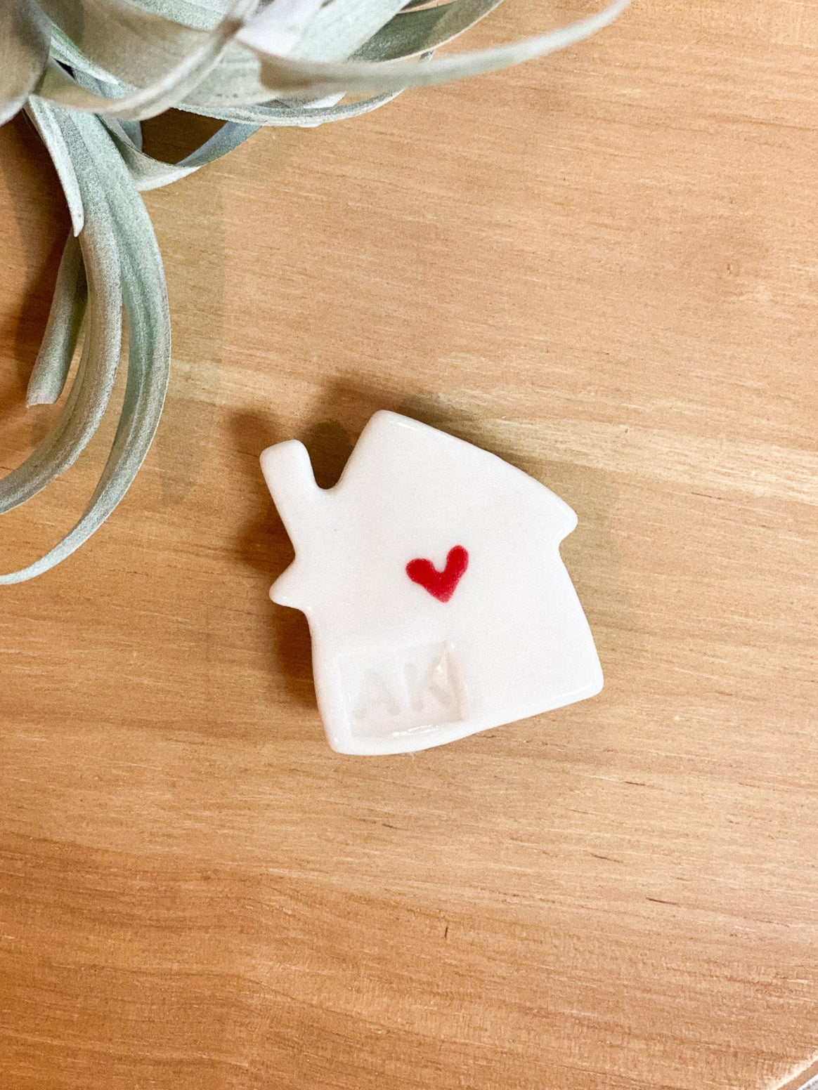 White house-shaped object with a red heart on a wooden surface with a plant in the background