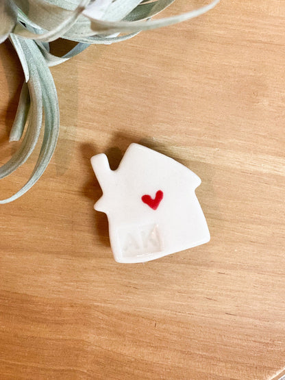 White house-shaped object with a red heart on a wooden surface with a plant in the background