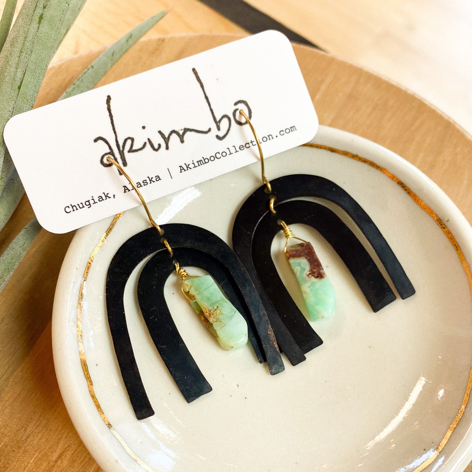 Black and green earrings on a white dish with 'akimbo' branding