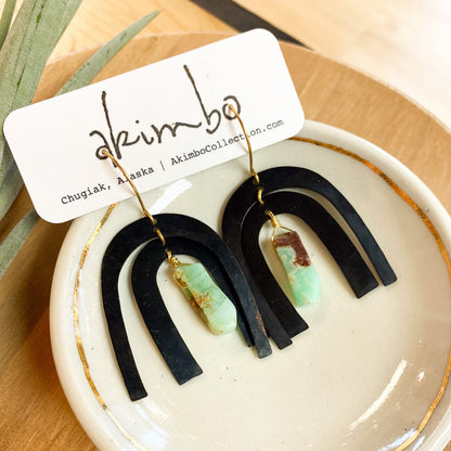 Black and green earrings on a white dish with 'akimbo' branding