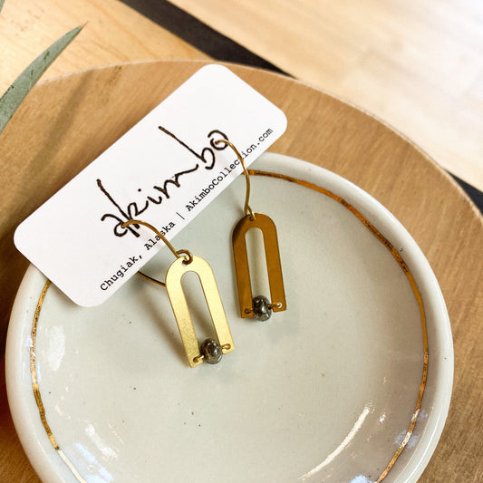 Gold earrings on a white dish with a brand tag on a wooden surface