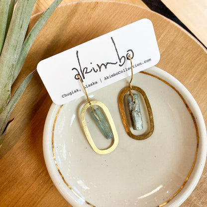 Gold and green earrings on a white dish with 'akimbo' branding