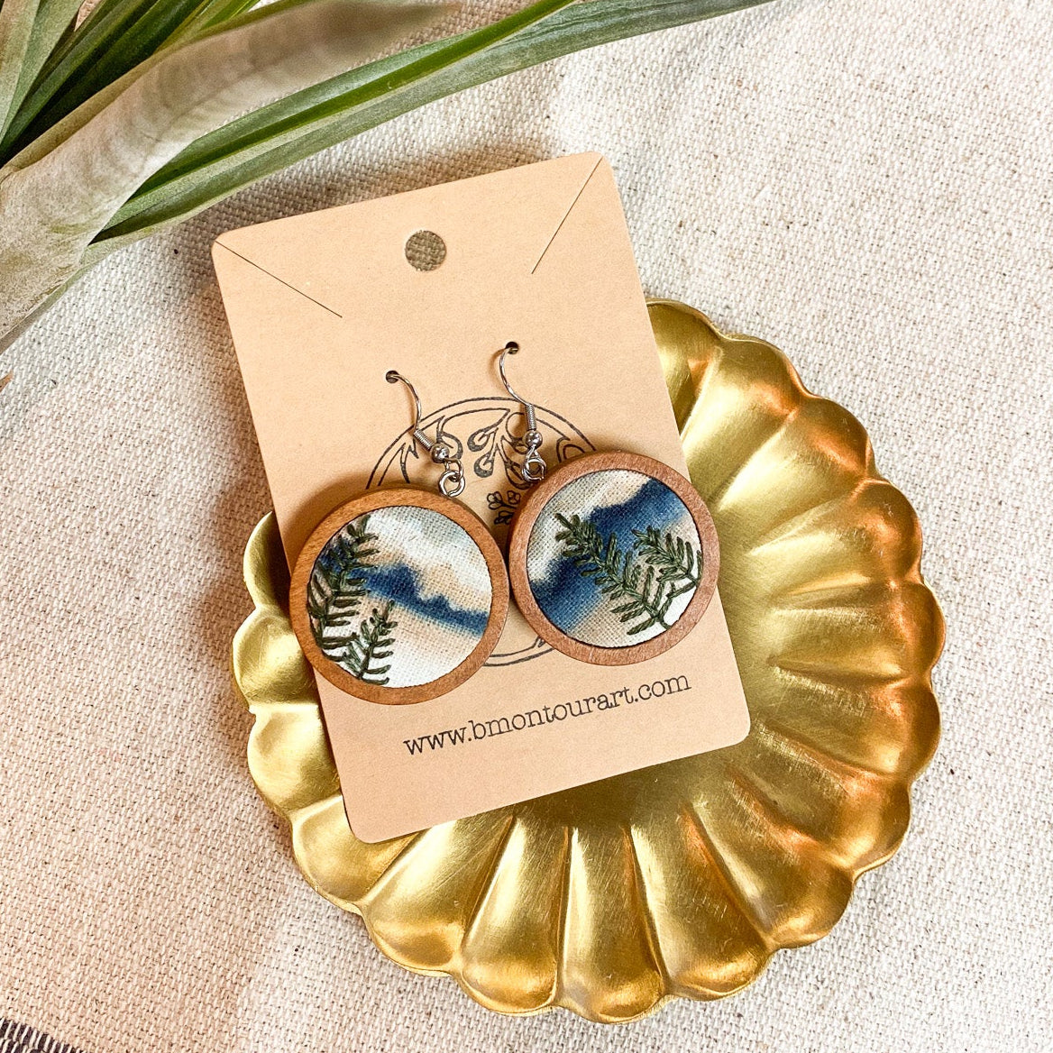Pair of earrings on a gold stand with a plant and fabric background