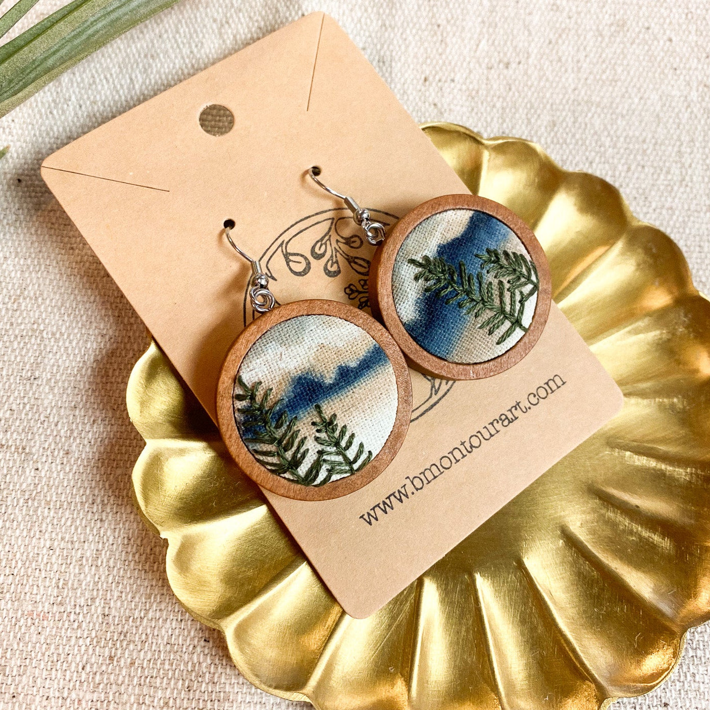 Pair of earrings with nature-themed design on a gold dish with a beige background