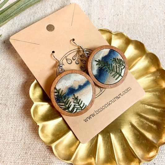 Pair of earrings with nature-themed design on a gold dish with a beige background