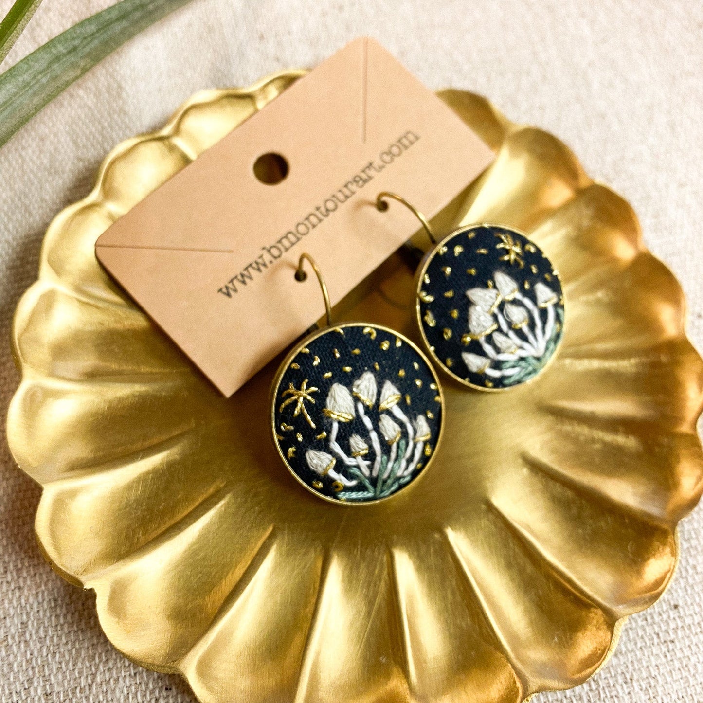 Pair of earrings on a gold dish with a beige background