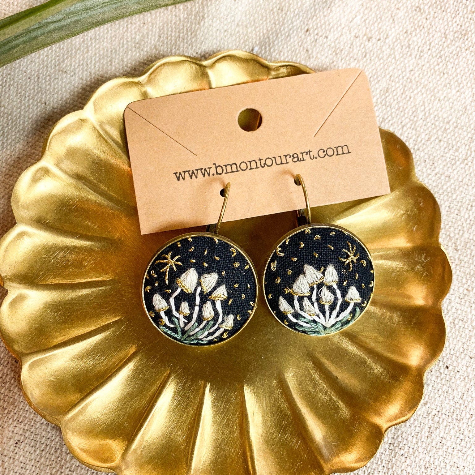 Gold dish with black and white floral earrings and a brand card on a beige background