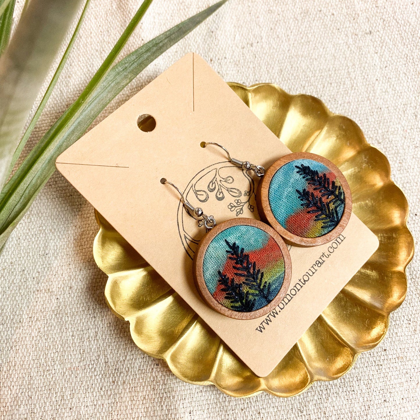 Wooden earrings with nature-themed design on a gold stand with a beige background