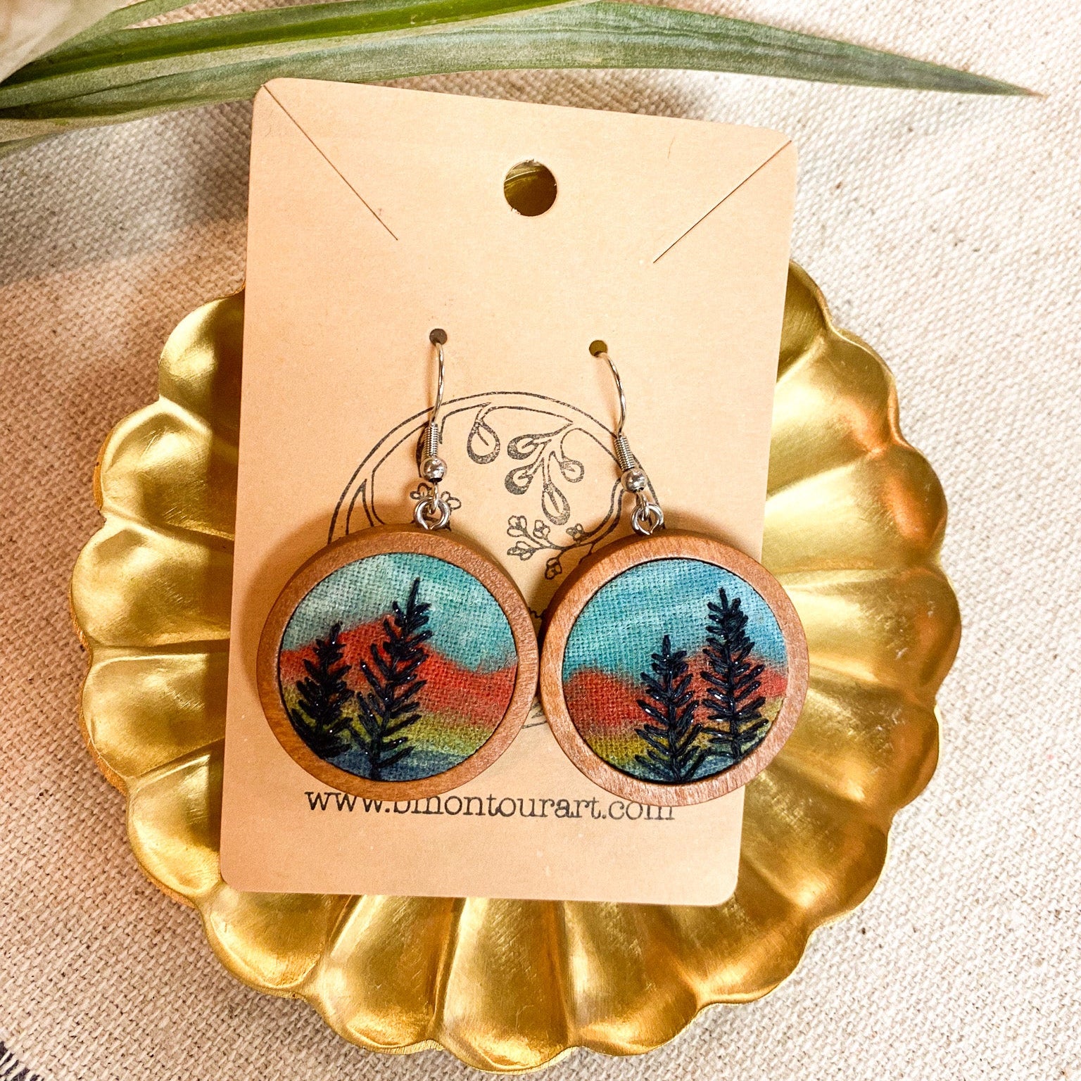 Earrings with nature-themed design on a gold stand and beige background