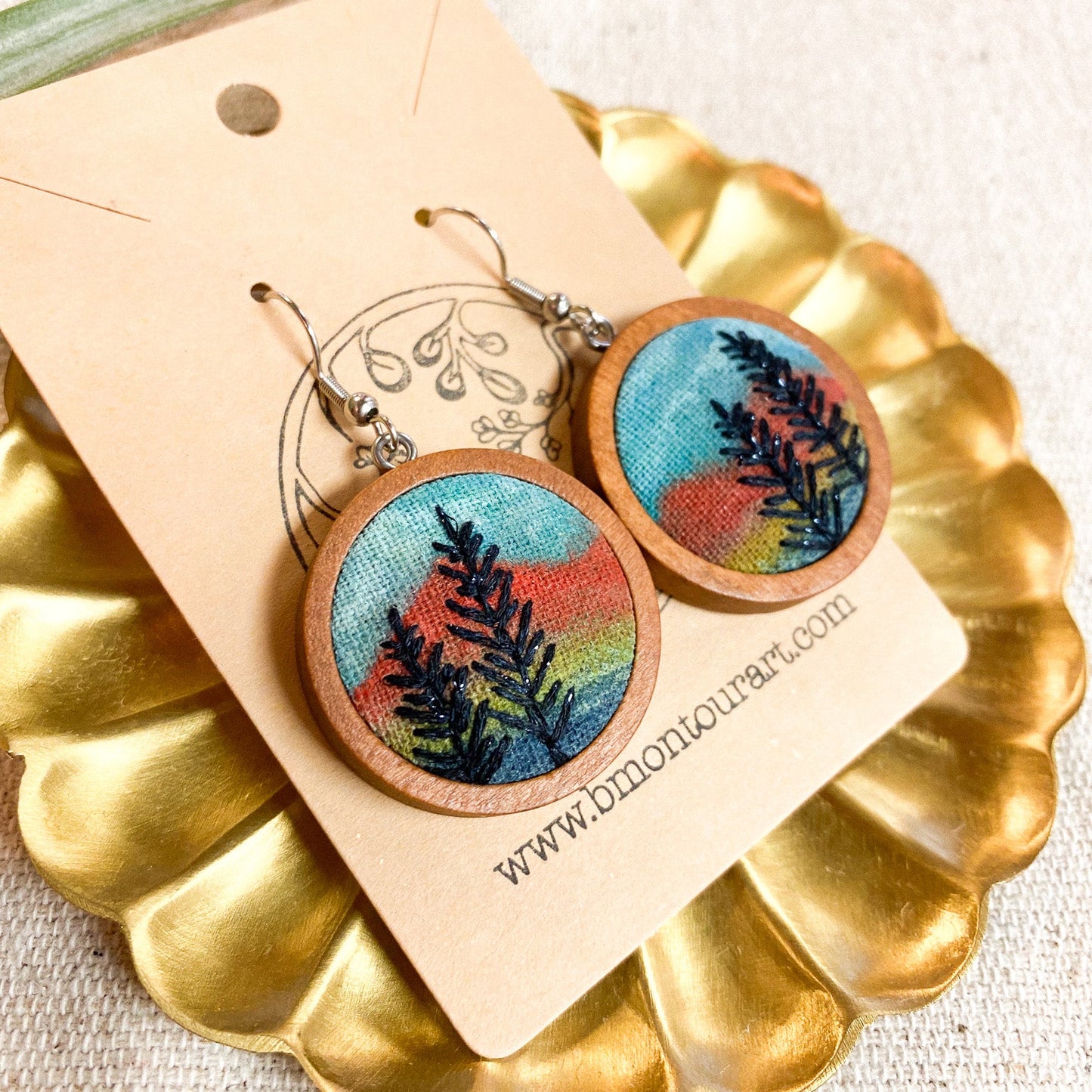 Wooden earrings with nature-themed design on a gold stand with a beige card.