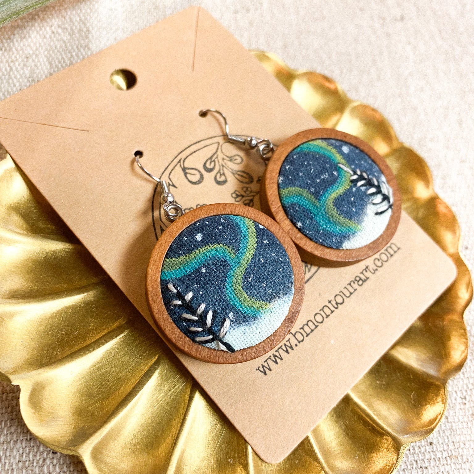 Wooden earrings with blue and green design on a gold stand with a beige card.