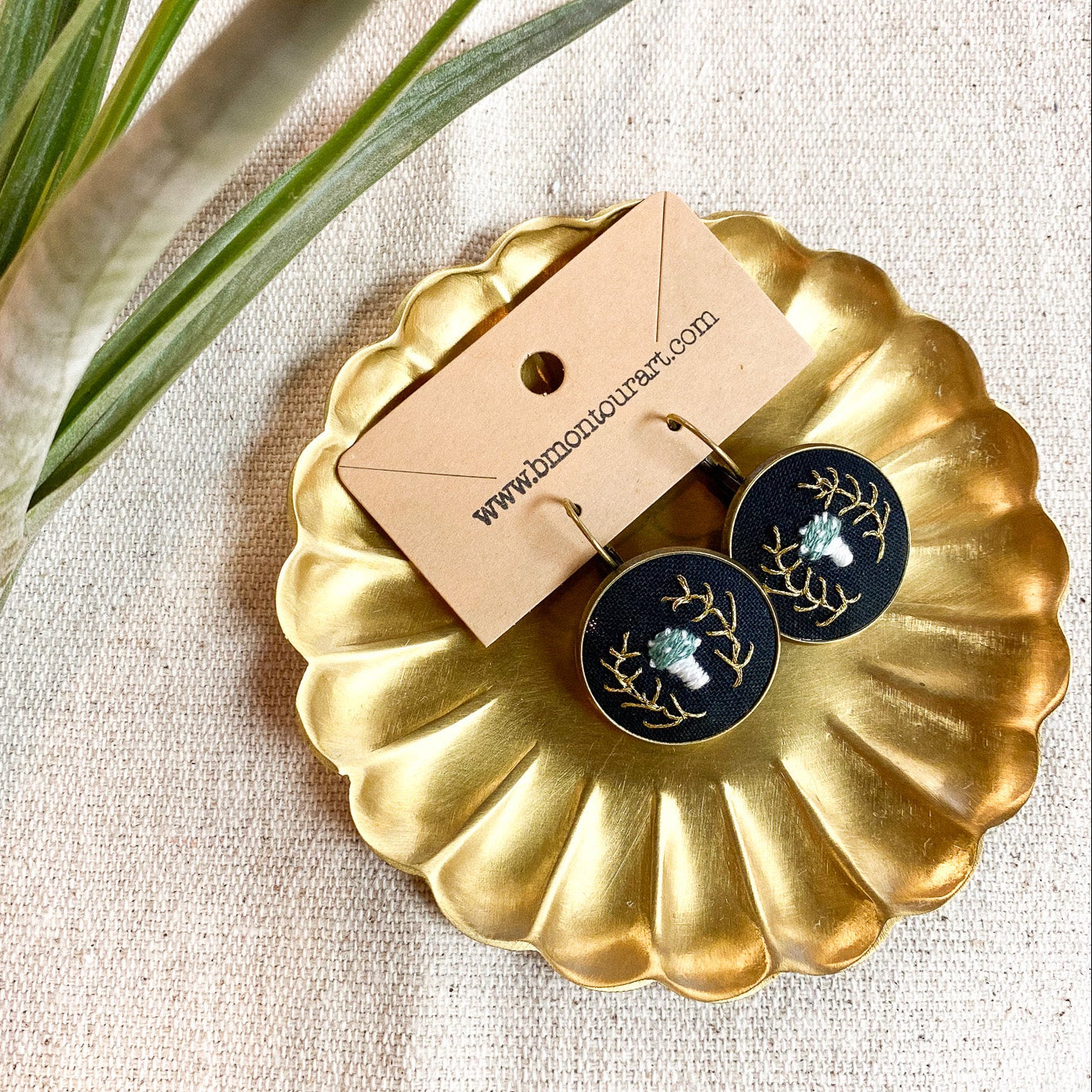 Gold decorative plate with black and gold earrings and a brown card on a textured surface.